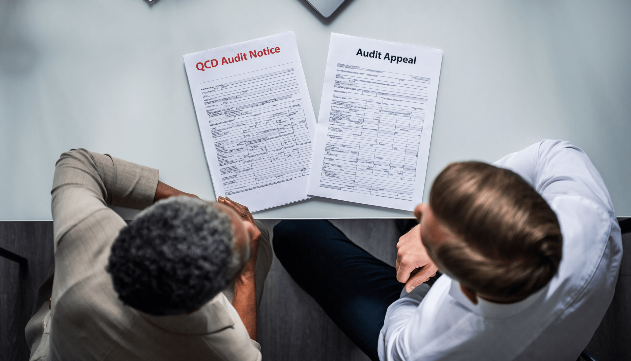 Older woman and young male accountant sitting at a desk looking at a QCD audit notice and an audit appeal form